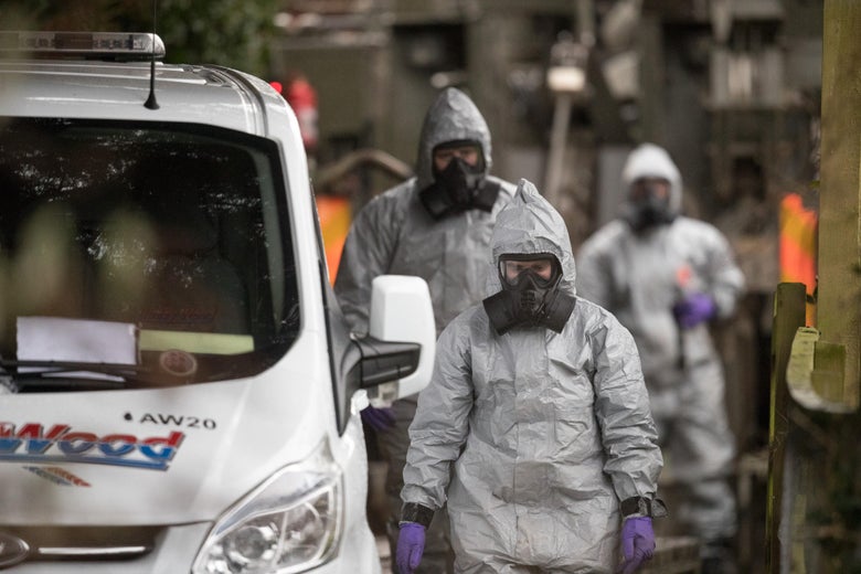Investigators in protective clothing walk near a white van.
